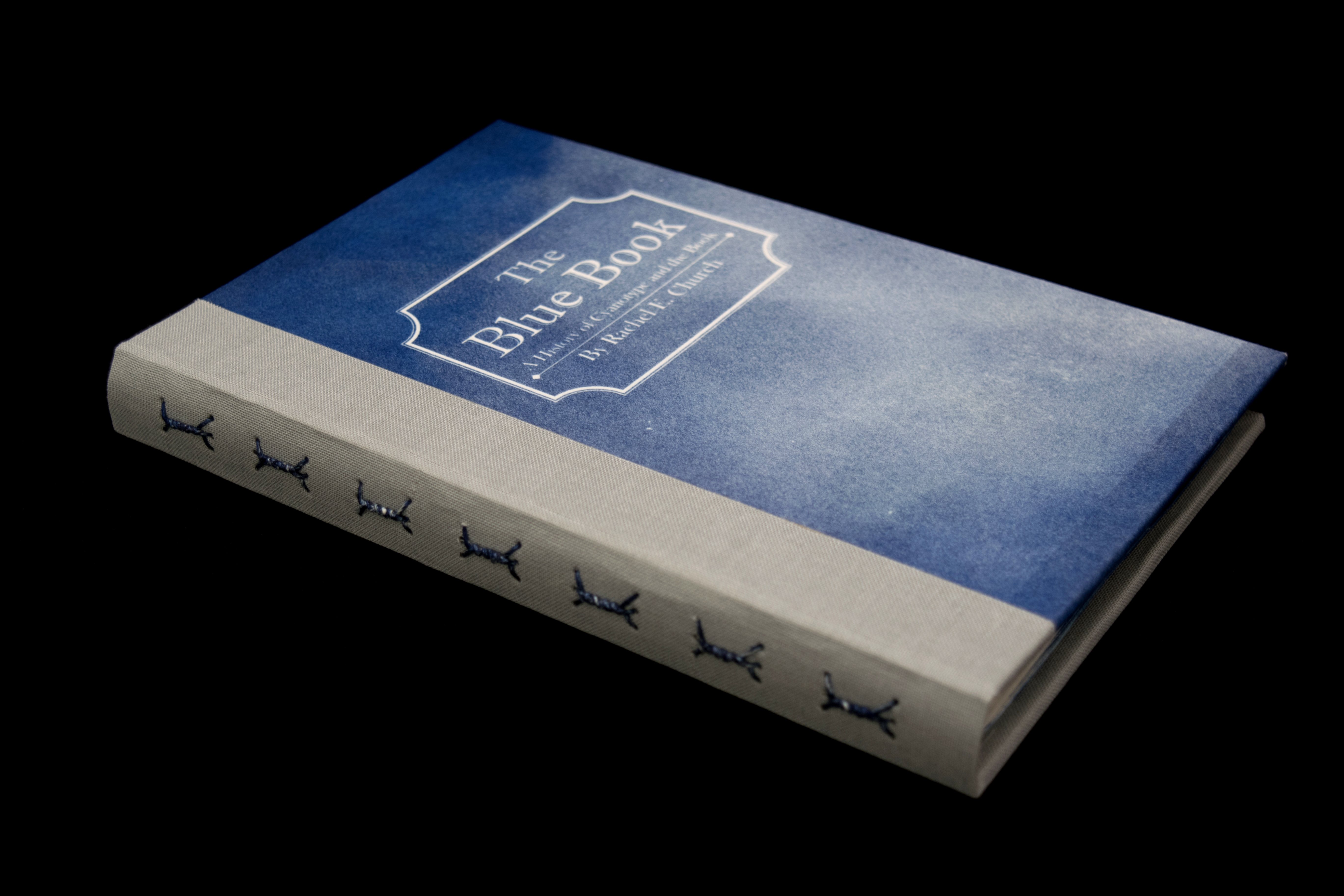 Blue book cover reads The Blue Book, A history of cyanotype and the Book by Rachel E. Church. Spine shows exposed decorative stitching