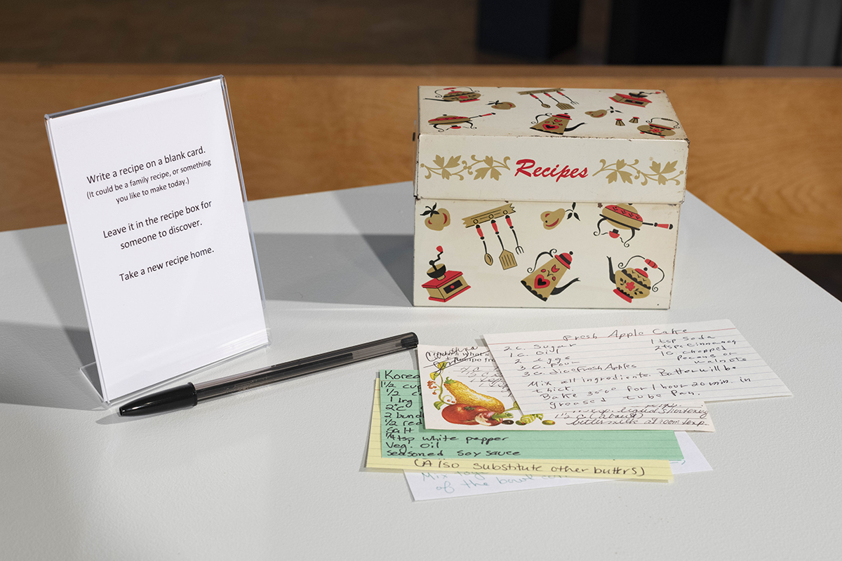 recpie box, recipe cards, pen, and a sign that reads "White a recipe on a blank card. Leave it in the recipe for for someone to discover, Take a new recipe home."