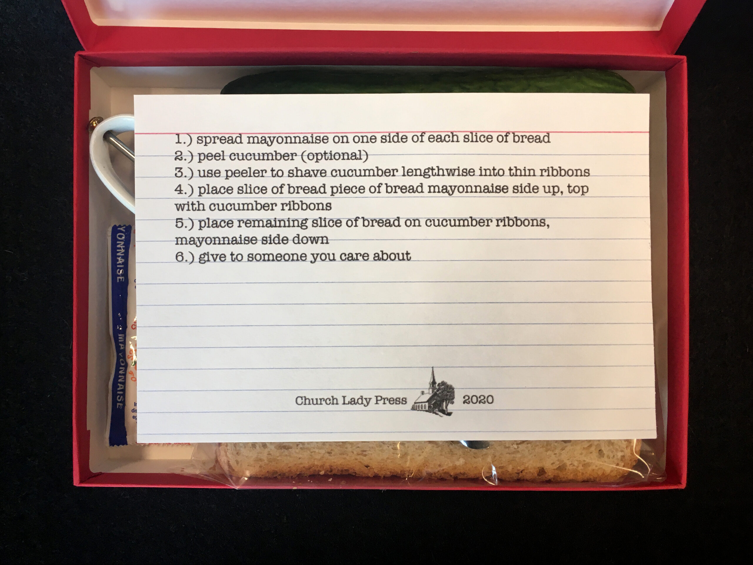 Open box with instruction card that reads: Spread Mayonnaise on one side of each slice of bread. Peel cucumber (optional) Use peeler to shave cucumber lengthwise into thin ribbons. Place Remaining slice of bread on cucumber ribbons, mayonnaise side down. Give to someone you care about.