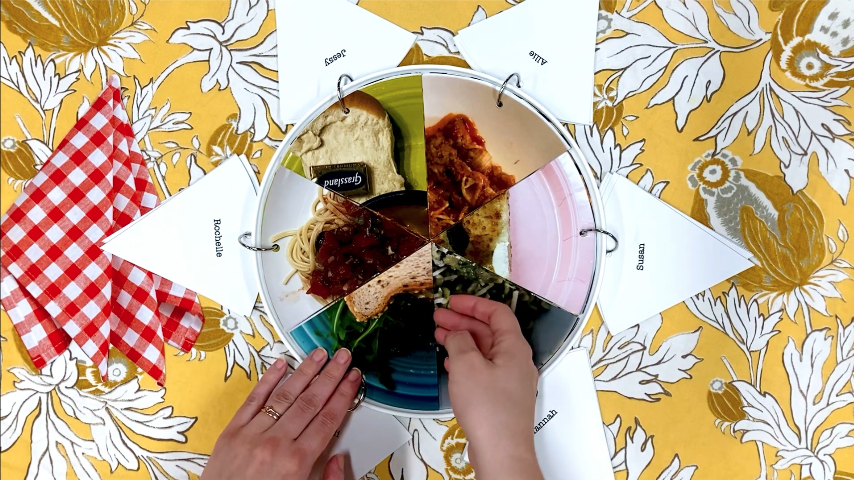 hands opening the pie shaped pages bound to a plate with a binder ring. Each page contains 1/6 of the image of a different meal on a plate. 